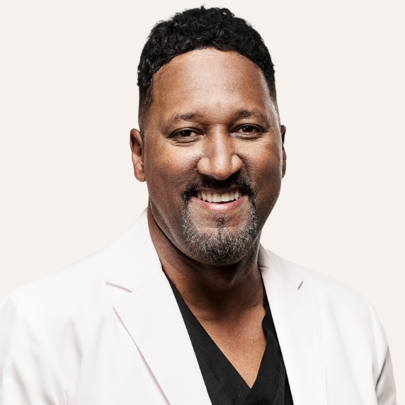 Male Heartland Supported Doctor wearing a white lab coat and dark scrubs