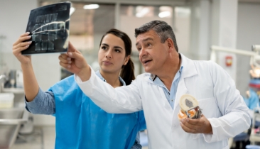 An middle aged doctor pointing something out on a dental x-ray that a hygienist is holding