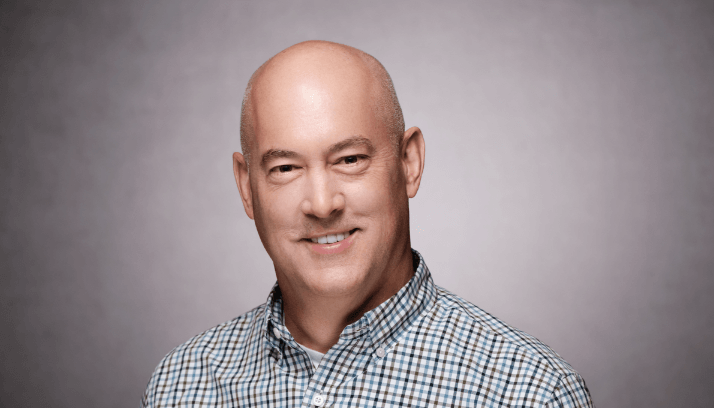 Male business professional in a pale green windowpane shirt against a light brown background