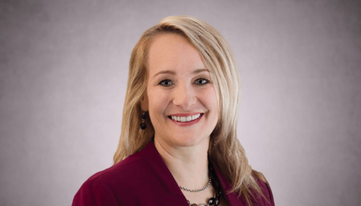 Female business professional in a maroon business suit against a light brown background