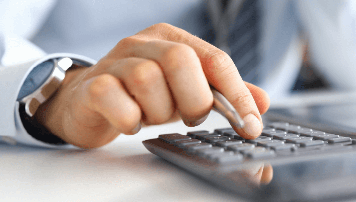 Closeup of an accountants hand holding a pen and typing on a calculator