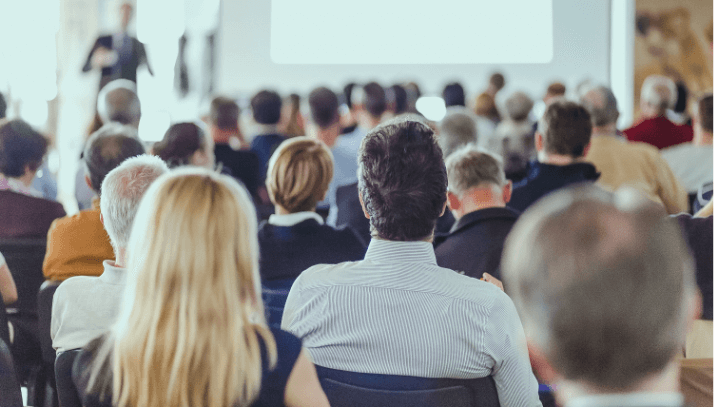 Rear shot of an audience of seated professionals listening to a presentation