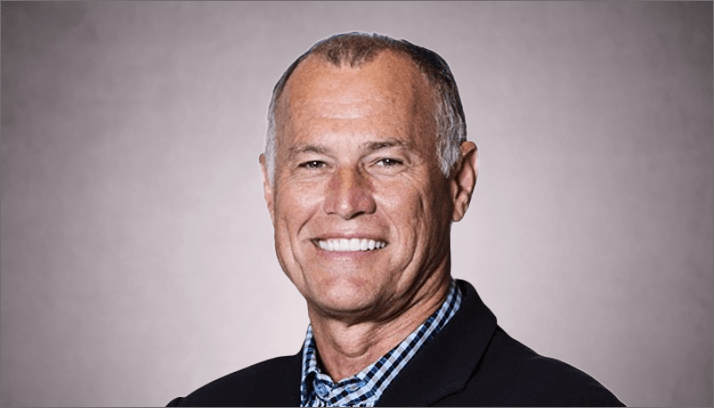 Male business professional in a light blue shirt and dark blue jacket against a light brown background