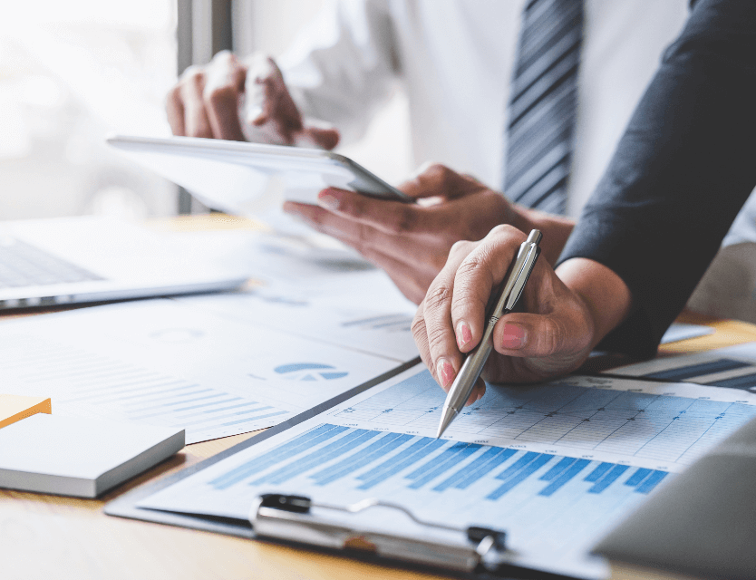 Close up of a professional woman's hand holding a pen pointing at graphs on a clipboard.