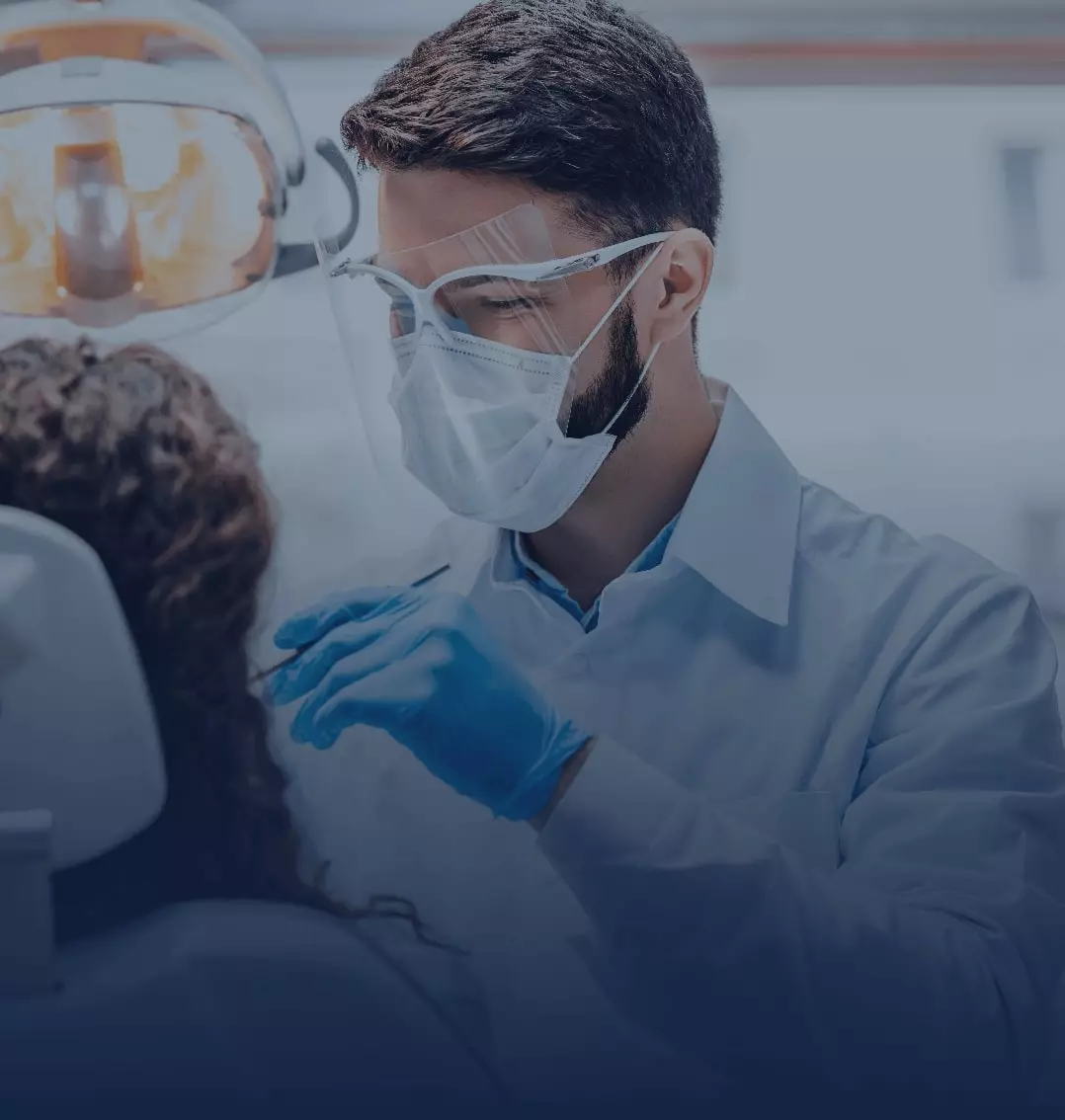 Masked male dentist wearing blue surgical gloves cleaning a female patients teeth