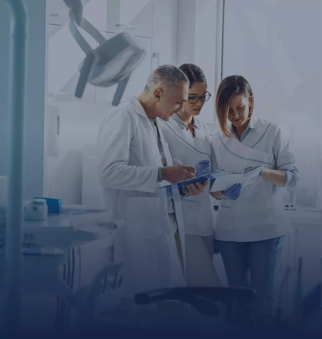 Group of three dentists in lab coats reviewing a patients chart